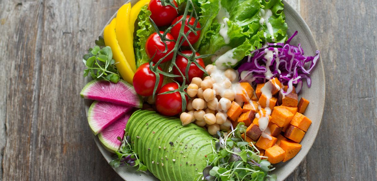 Dish with healthy vegan meal containing chick peas, tomatoes, avocado, pumpkin, red cabbage, yellow pepper, salad and cress